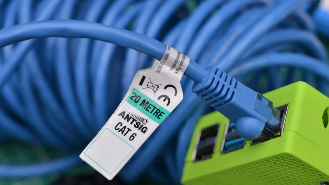 A detailed close-up shot of a blue Cat 6 Ethernet cable plugged into a vibrant green device. The image features a shallow depth of field, emphasizing the cables texture and the crispness of the connector. The contrasting blue and green colors create a visually striking composition, perfect for tech-related projects or website backgrounds.
